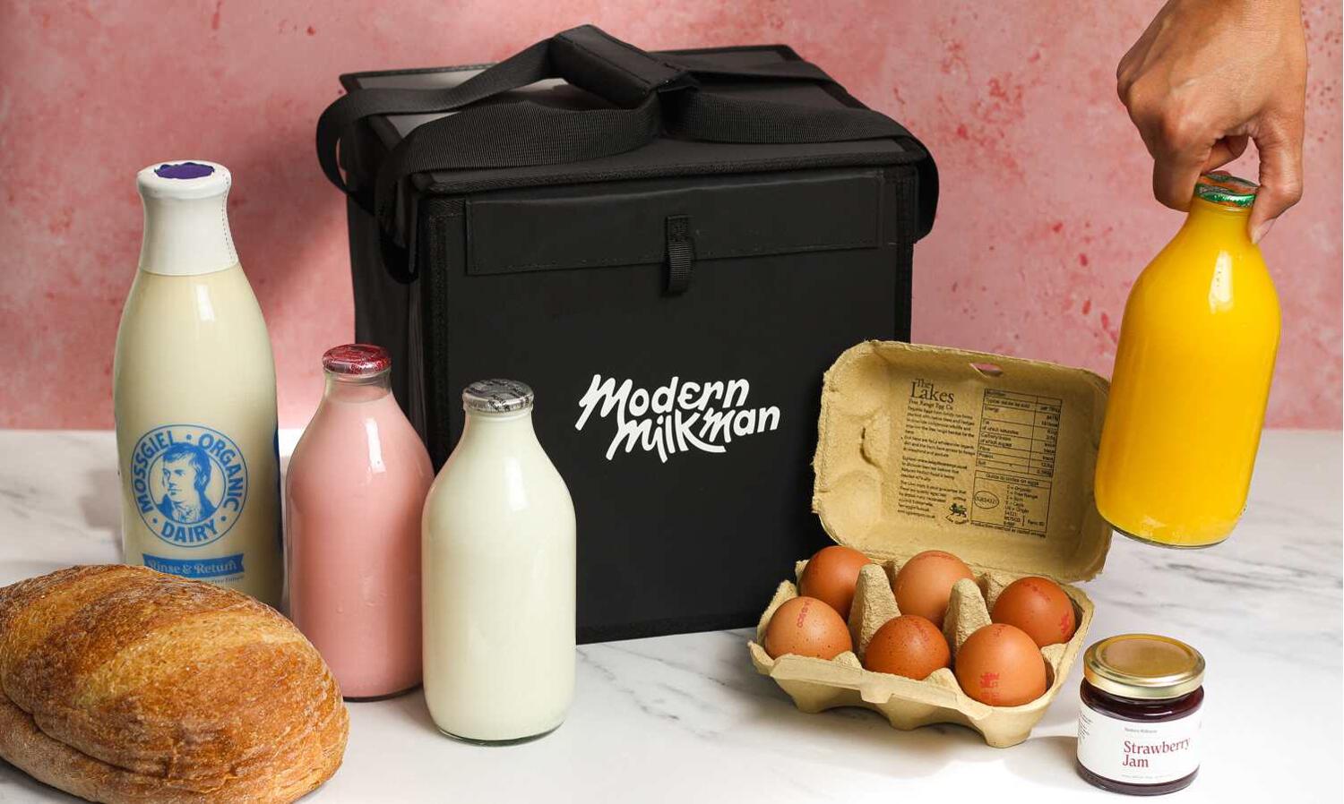 Modern Milkman discount codes banner showing a black branded cool bag surrounded by milk, orange juice, eggs, jam, and bread