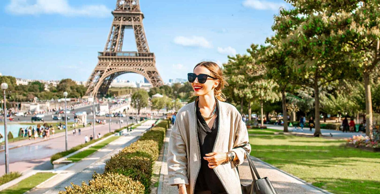 Musement offers page banner - A woman in Paris smiling with the Eiffel Tower in the background