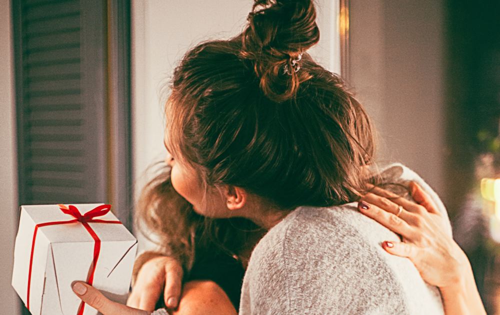 Erwachsene Frauen umarmen sich mit Geschenk