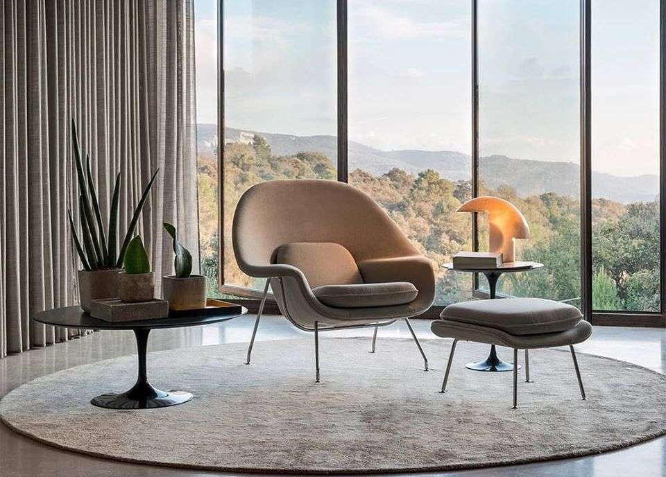 Fauteil et tables basses sur tapis rond beige devant une baie vitrée