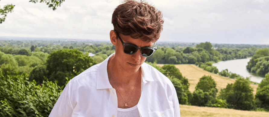 Neem London page banner - A man in a white shirt and wearing sunglasses, in front of a countryside scene