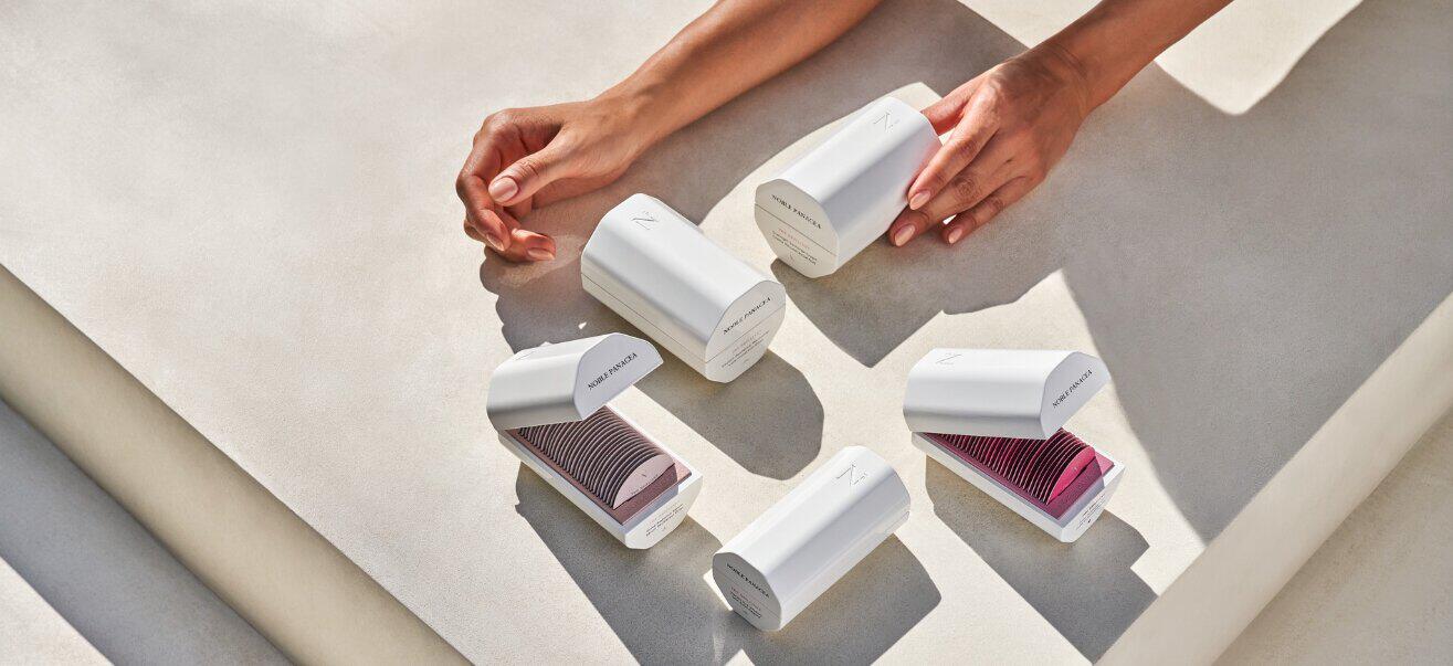 Noble Panacea offers banner featuring a selection of white packaging on a stone surface with arms reaching for the products