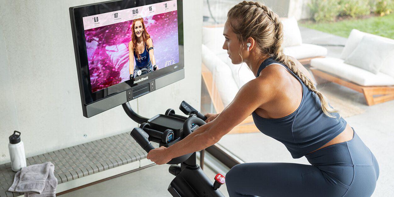 NordicTrack deals page - Woman on a large exercise bike watching a fitness class on an attached monitor