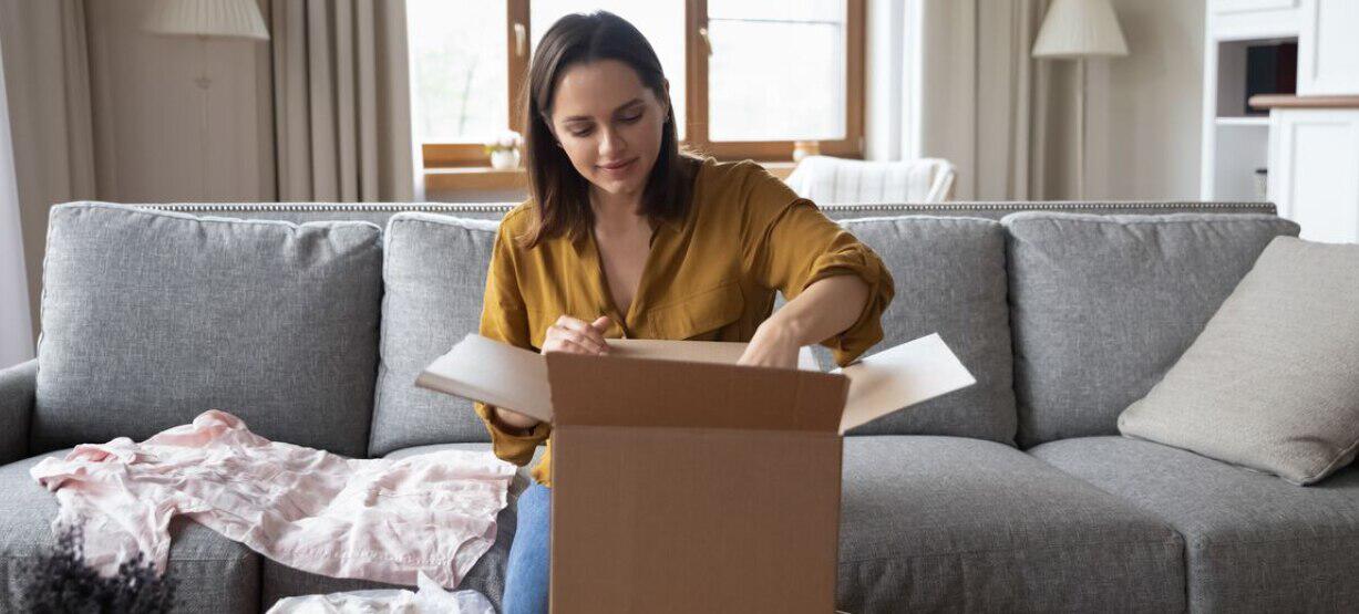 Parcel2Go more ways to save banner. Image features a woman sitting on a grey sofa packing a cardboard box with clothing