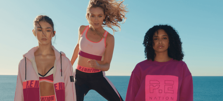 P-E Nation savings page banner. Image features 3 women of different ethnicities wearing pink branded clothing in front of seaside background