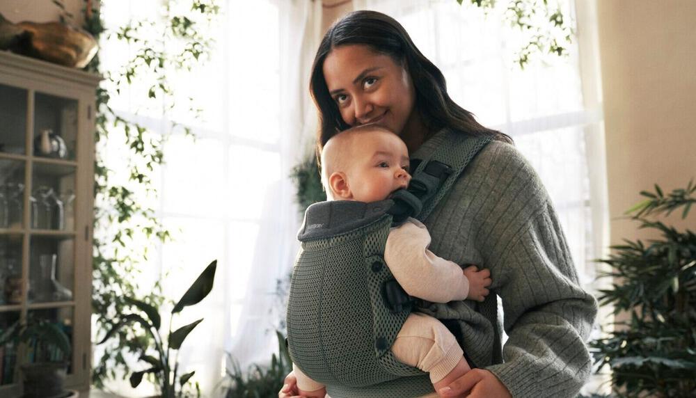 Femme qui porte son enfant dans un porte-bébé BabyBjörn vert sapin
