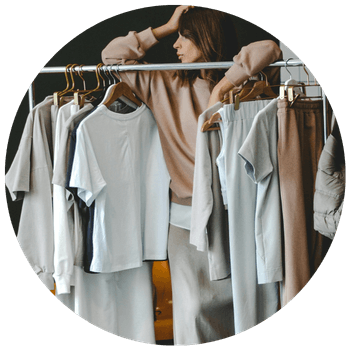 Woman leaning on a clothes rail holding neutral colour clothing