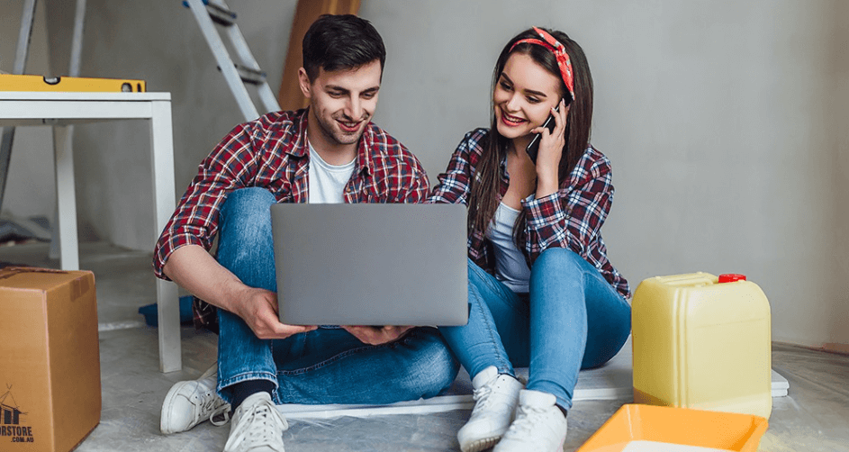 Renovator Store deals page banner - A man and woman sitting on the floor looking at a laptop with DIY products surrounding them