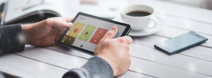 Homme qui tient une tablette sur une table avec une tasse de café et un téléphone