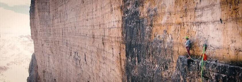 Bergsteiger mit Salewa Ausrüstung steht am Rande einer Klippe an einer Bergwand – Banner der Salewa Gutscheinseite