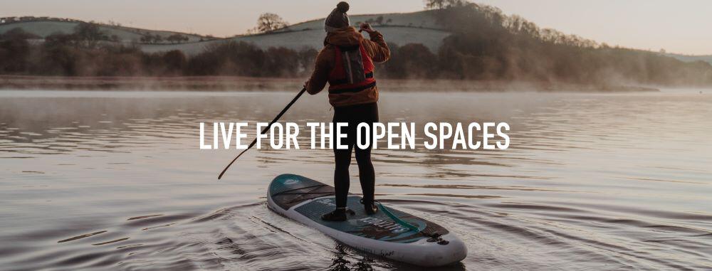 Saltrock clothing and board ad banner: woman in a wetsuit stood on a paddleboard. Text reads: Live for the open spaces