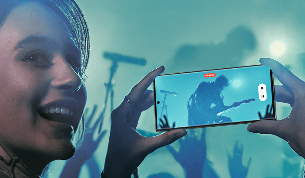 Samsung new year deals image - Woman in a club holding up a smartphone showing the on stage musician