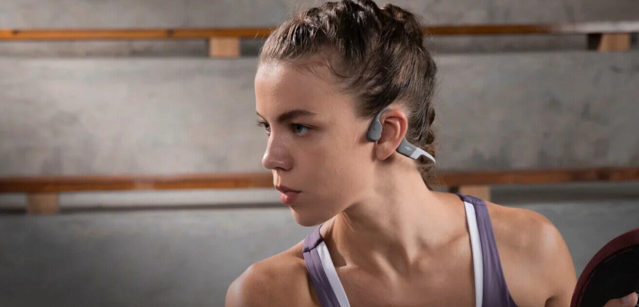 SHOKZ deals page image showing a close up headshot of a woman in the gym wearing open-ear headphones