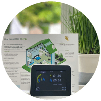 A smart meter displaying sitting on a table with an instructions booklet and plant behind