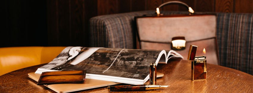 Table en bois avec magazine ouvert, briquet en or, stulo plume et malette en cuir marron ST Dupont