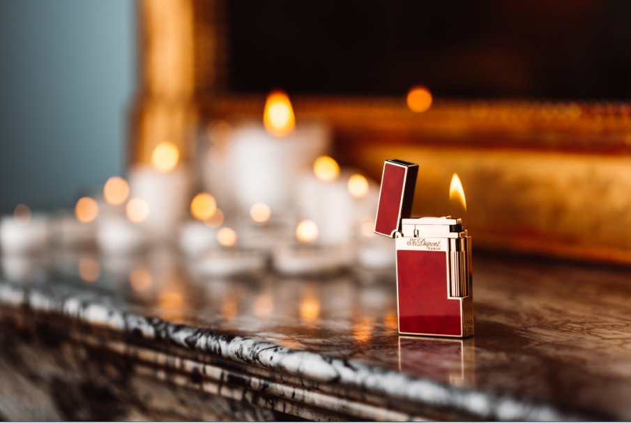Briquet marron ST Dupont sur une cheminée en marbre devant un miroir et des bougies