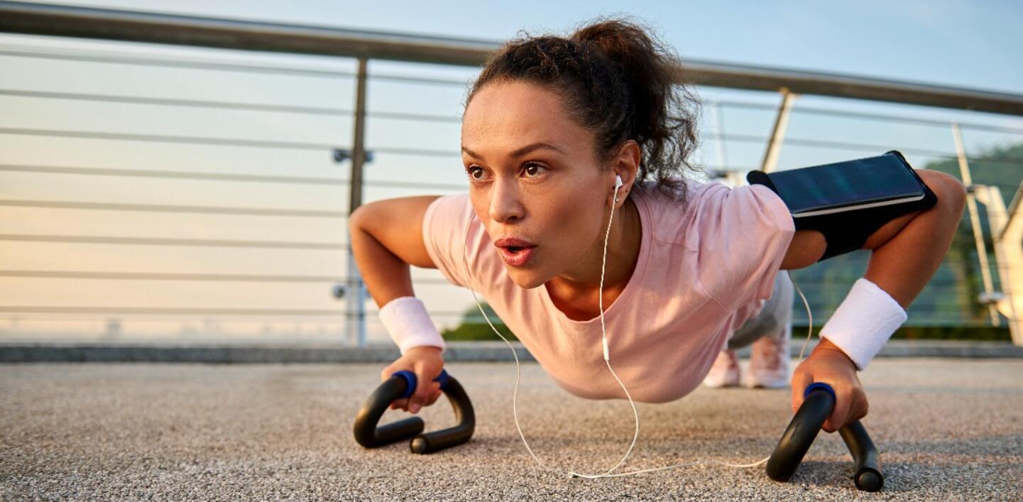 Sweatband savings guide banner - Imafe shows a woman doing press ups outside using hand support and and a fitness monitor on arm