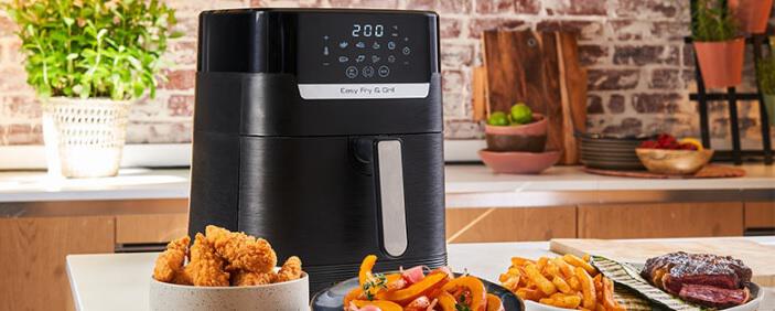 Tefal Heißluftfritteuse auf einer Küchenablage mit zubereiteten Speisen davor als Banner für die Tefal Gutscheinseite