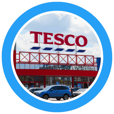 Tesco storefront image showing a large Tesco logo on a superstore with parked cars in front
