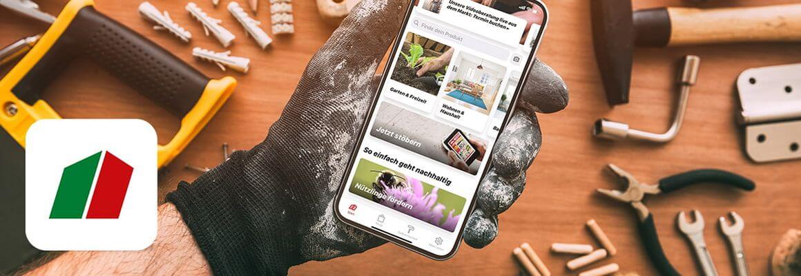 Smartphone mit geöffneter Toom App in Hand mit Arbeitshandschuh