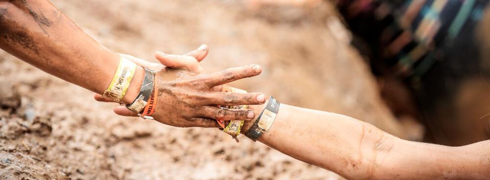 Zwei Tough Mudder-Teilnehmer überklettern gemeinsam ein Hindernis