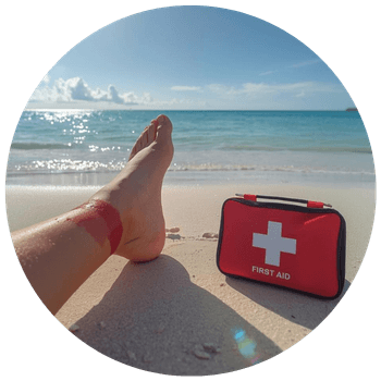 Travel injury image showing a hurt leg on a beach with a red first aid pack sitting on the sand