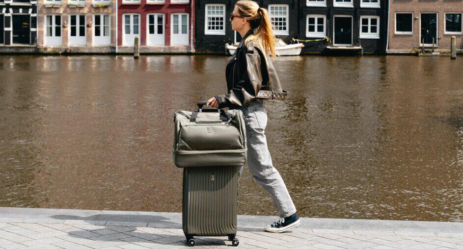 Travelpro how to save money tips banner - A woman in leather jacket pushing a luggage case alongside a scenic canal
