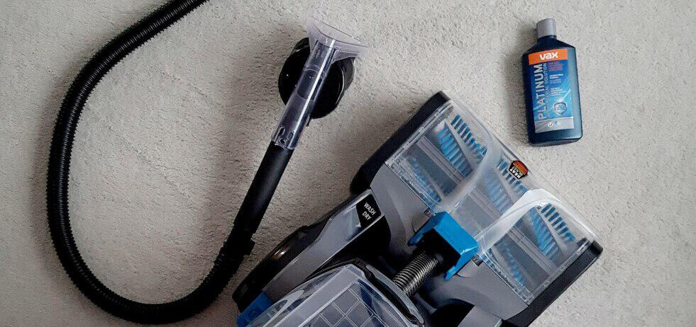 Vax page banner featuring a cleaning device and soloution bottle lying on a pale carper