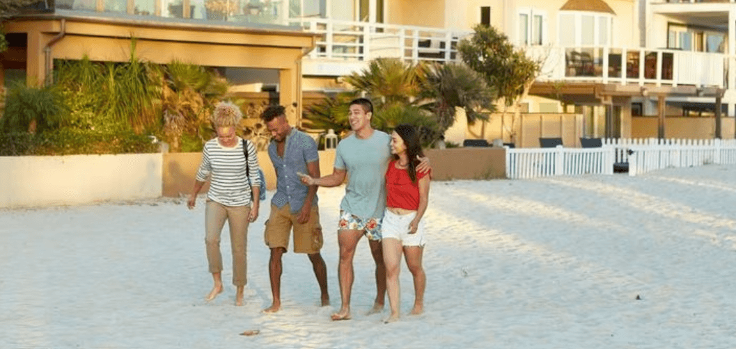 VRBO beach holidays image showing a group of friends walking on the sand in front of holiday lets
