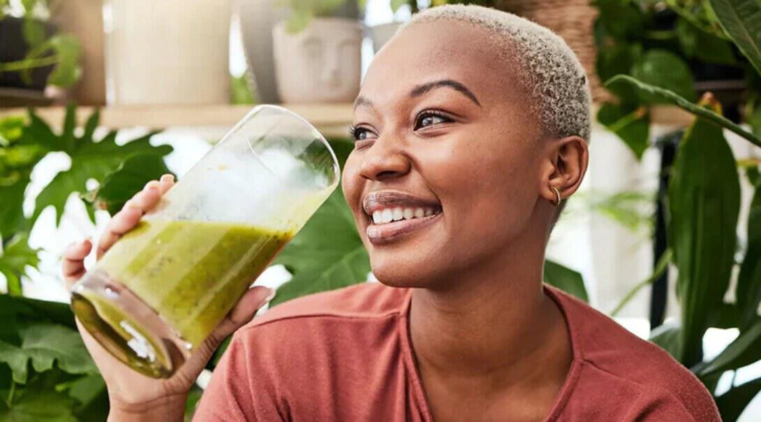 W-Wellness how to save guide - A smiling woman holding a large glass of a green wellness drink