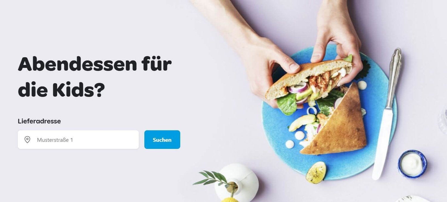 Suchmaske für die Lieferadresse zum Essen-Bestellen bei Wolt. Zu sehen sind zudem ein Paar Hände und ein Teller mit einem Döner.