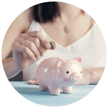 A woman putting a coin in a pink piggy bank while sat at a blue table