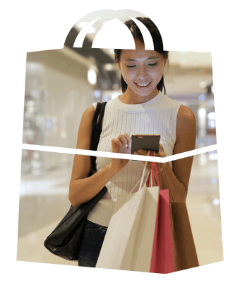 Woman shopping in a shopping centre setting. She is using a mobile and smiling. The image is contained within a shopping bag shaped frame.